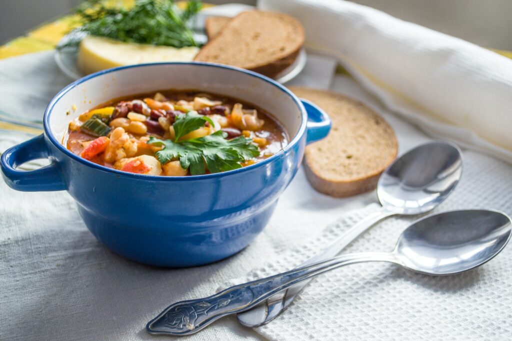  vegetable and bean soup in a blue bowl surrounded by 2 spoons and 2 slices of brown bread (Morphy Richards vs Ninja Soup Makers)