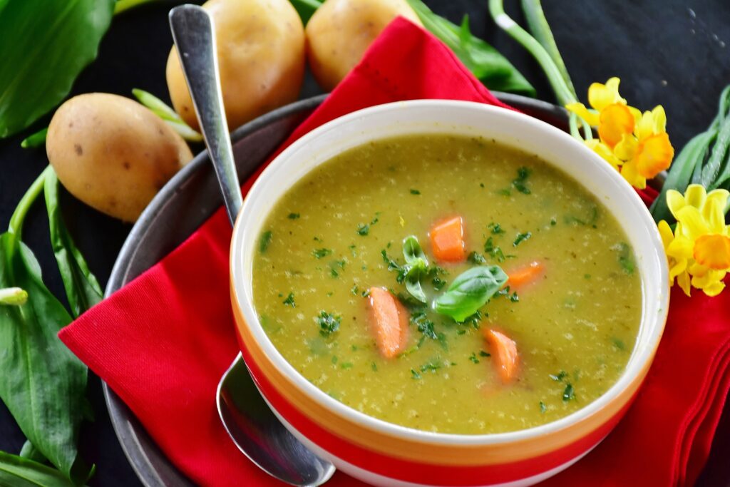 bowl of vegetable soup on a plate with a red napkin, with 3 boiled potatoes alongside