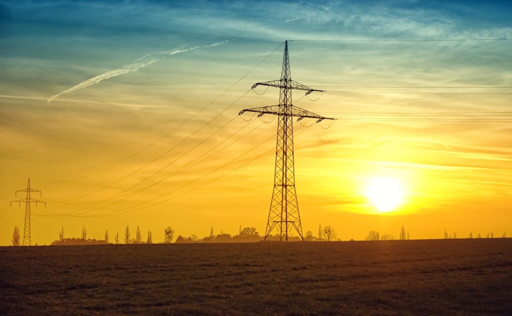 electricity poles in a field with the setting sun behind